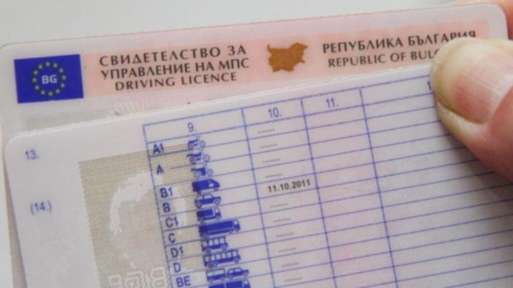 Close-up of a Bulgarian driving license showing vehicle category icons and the issue date near the top edge, held by a finger.