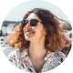 Portrait of a woman with curly hair wearing sunglasses, smiling outdoors on a sunny day